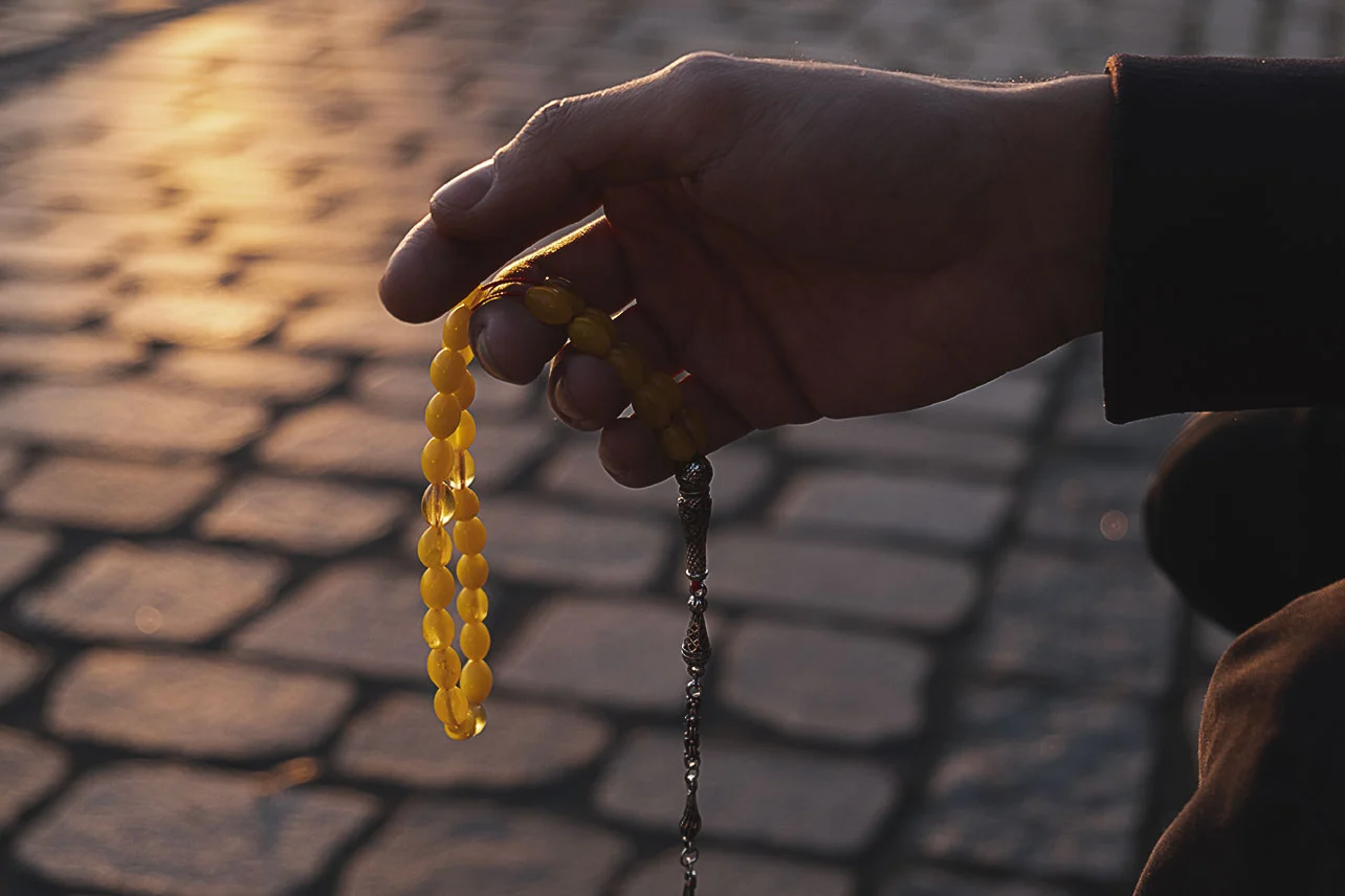 Nahaufnahme einer Hand mit einer Misbaha, einer muslimischen Gebetskette aus gelben Perlen. Die Kette wird auf eine Art gehalten, als ob sie gerade benutzt wird.